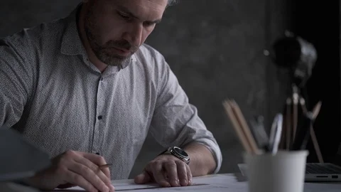 Architect draws a plan on paper while sitting at a table in a dark office. Stock Footage 107330544