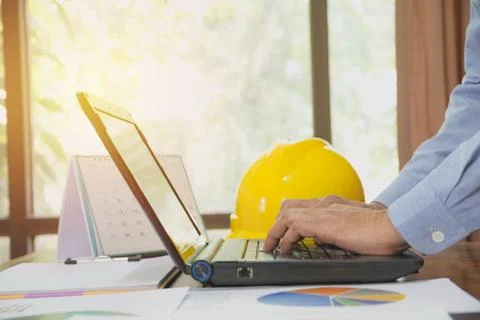 Architect engineer using laptop for working with yellow helmet on desk. Stock Photos