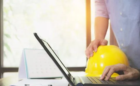 Architect engineer using laptop for working with yellow helmet on desk. Stock Photos
