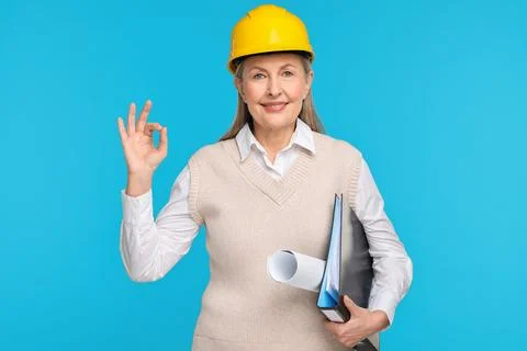 Architect in hard hat with draft and folder showing ok gesture on light blu.. Stock Photos