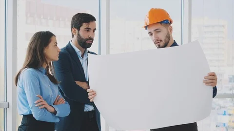 An architect in a helmet shows an object plan to his colleagues. Stock Footage 102389615