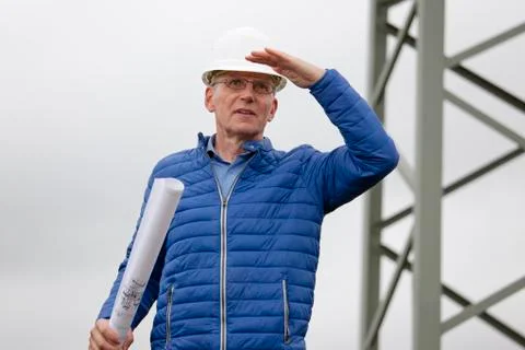 Architect or engineer with hard hat and blueprint in his hand looking out  fo Stock Photos