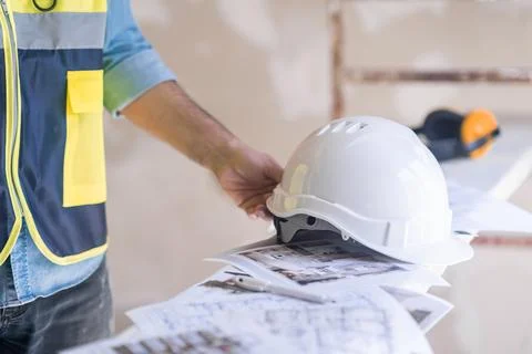 Architect reaching hand to take hardhat on heap of project papers at Stock Photos