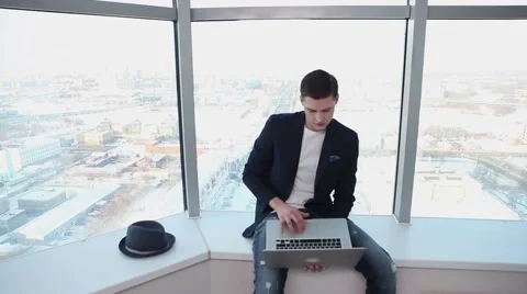  architect sits on a background of a large window with a laptop in his hand Stock Footage 59791135