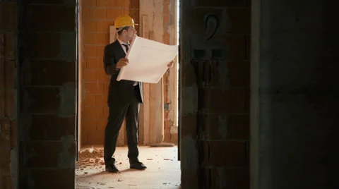 Architect standing in house under construction with building plan Stock Footage 24501047