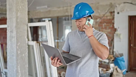 Architect using laptop talking on smartphone at construction site Stock-Footage 247386876