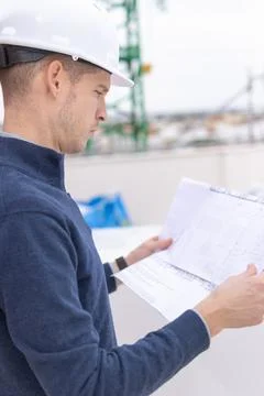 Architect wearing a white hard hat and blue pullover, reviewing constructio.. Stock Photos