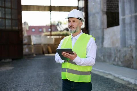 Architect in white hard hat and reflective vest standing, working on digital Stock Photos
