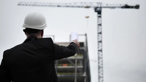 Architect in white helmet points out something with his hand holding drawings in Vidéo 275288581