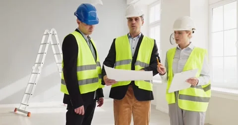 Architects and workers review building plans in hard hats at renovation site Stock Footage 334692412
