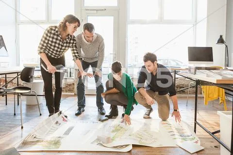Architects Discussing Blueprints On Wooden Floor