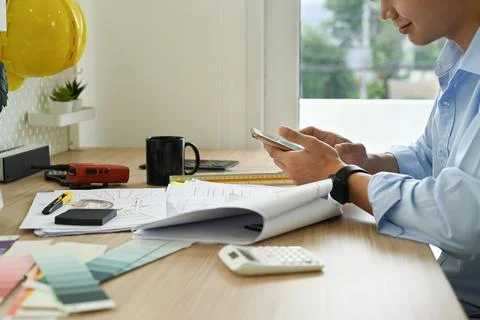 Architects man using mobile phone, working on design of a construction plan at Foto stock
