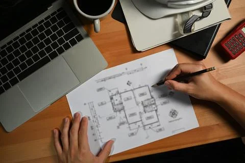 Architects man working on construction plans and using laptop on wooden desk Stock Photos