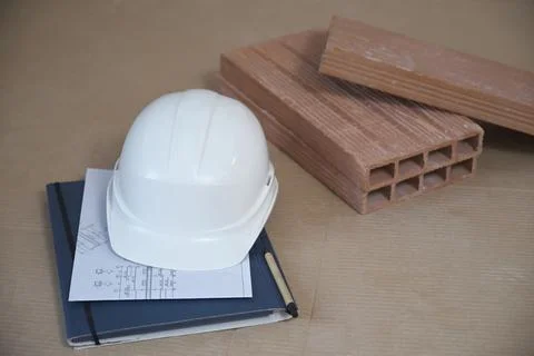 Architectural blueprints, stack of bricks, construction hard hat on cardboard. Stock Photos