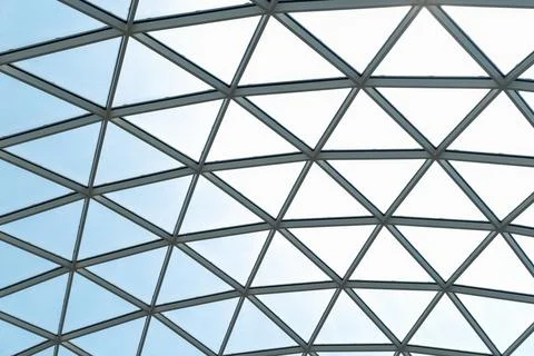 Architectural glass structure with a geometric triangular pattern on a blue s 스톡 사진