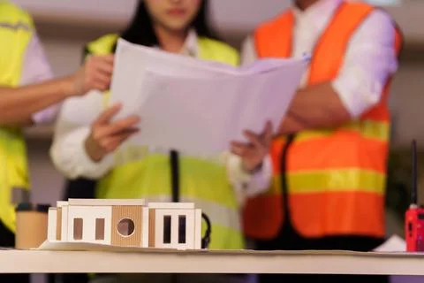 Architectural house model on table with engineers reviewing blueprints in Stock Photos