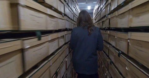 An archivist walks between rows of shelving units filled with folders and boxes Stock Footage 344888733