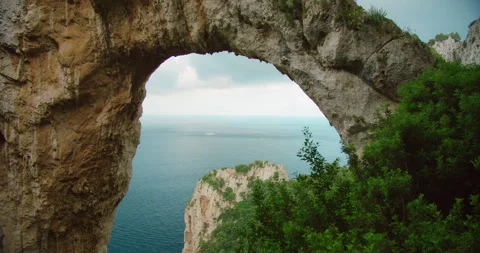 Arco Naturale stone arch frames the sea and cliffs on summer day in Capri Italy Stock Footage 326018255