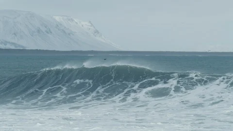 Arctic wave breaks with snow mountains in background 4K Stock Footage 128448235