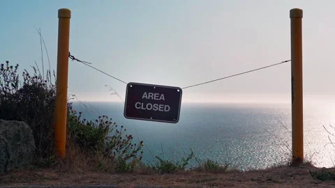Area closed sign waves in the wind overlooking ocean cliff Stock Footage 304249204
