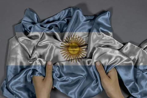 Argentina Flag Grasped by Hands Draped in Silk Across Grey Background Stock Photos