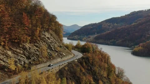 Arial drone of single car navigating a winding mountain road alongside a lake Stock Footage 330770612