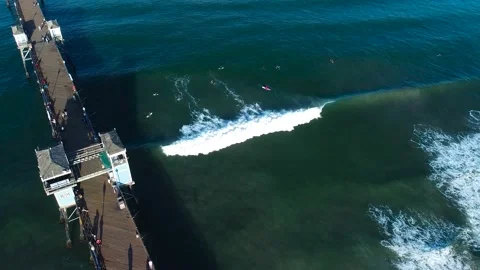 Arial shot of oceanside pier and surfers with wave breaking Stock Footage 217900010