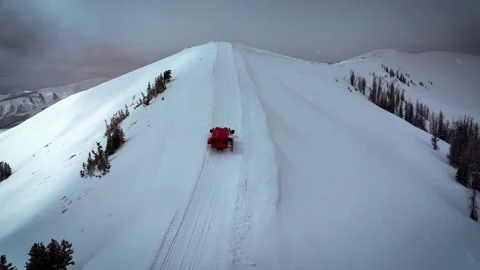 Arial shot of a snowcat as it plows along a mountain top in Idaho Stock Footage 230773406