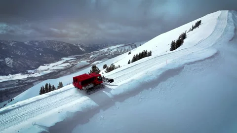 Arial tracking shot of a snowcat as it plows along a mountain top in Idaho Stock Footage 230772429