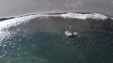 Ariel angle of peaceful waves roll into a black sand beach shore paradise Видео 103223167
