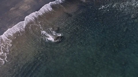 Ariel drone pull back of peaceful waves roll into a black sand beach shore Stock Footage 103223730