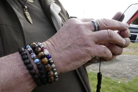 Arm of a man with bracelets operating a smartphone Fotos Stock