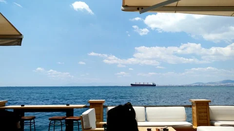 Armchairs and tables by the seafront, cargo ship at sea, Thessaloniki Greece Stock-Footage 114311229