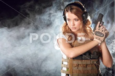 Armed blonde woman shoots with gun at a target in the darkness with smoke clouds Stock-Fotos