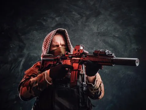 Armed soldier with hood and modern equipment aims a rifle Фото