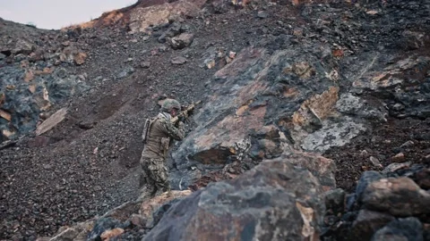 Armed soldier walking over large rocks in 4k UHD Stock Footage 145268132