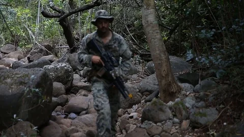 Armed U.S. Marine walking through dry river bed duirng jungle patrol Stock Footage 105289568