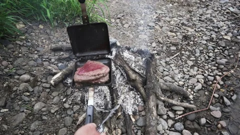 The arms of a person cooking steak on an open fire with a grill and knife Stock Footage 135071153