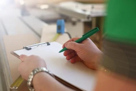 Arms of worker making notes on clipboard with green pen Stock Photos