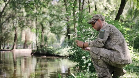 Army military soldier checking mobile phone in forest wearing camouflage uniform Stock Footage 265898396