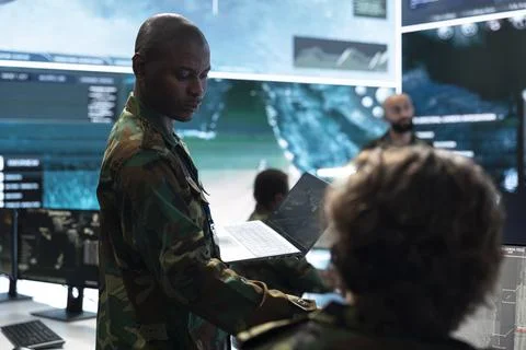 Army officer using laptop in command center and talking with personnel Stock Photos