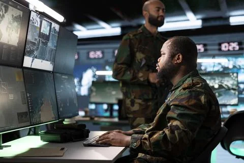 Army operator typing data while armed soldier guarding workstation Stock Photos