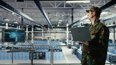 Army soldier in server farm uses artificial intelligence program on laptop Stock Footage 314804284