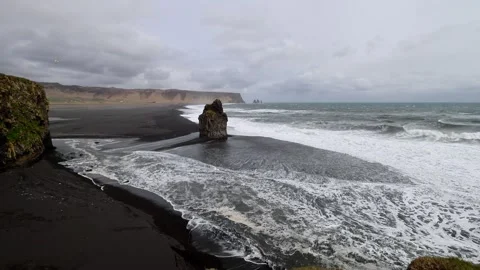 Arnardrangur basalt sea stack on Reynisfjara black sand beach with crashing o Stock Footage 339303956
