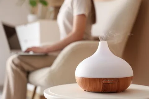 Aromatherapy diffuser emitting mist on a white table with a person working on Stock Photos