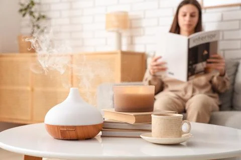 Aromatherapy diffuser emitting steam on a coffee table with a woman reading i Stock Photos