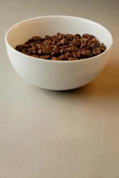 Aromatic coffee beans in a simple white bowl resting on a clean surface Foto stock