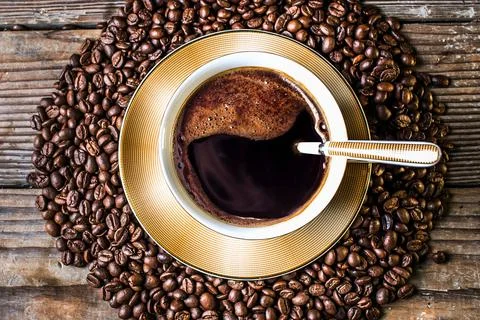 Aromatic coffee cup surrounded by freshly roasted coffee beans on wood Stock Photos