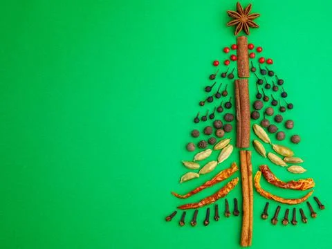 Aromatic spices as Christmas tree shape over green paper background. Stock Photos