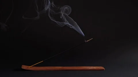The aromatic stick smokes in the stand on a black background. Incense for Video stock 124723459